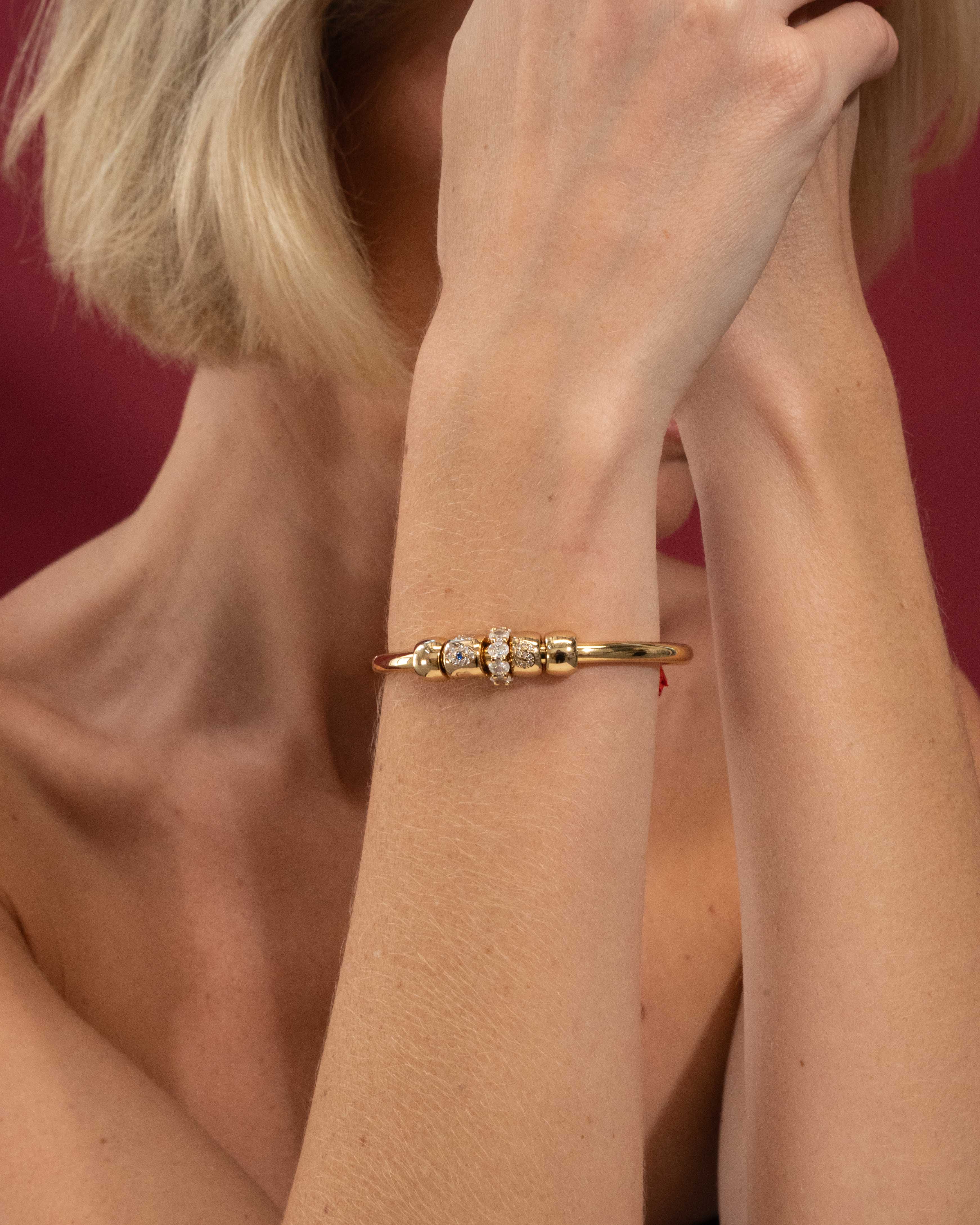 Gold bracelet with small diamonds on a person's wrist against a red background