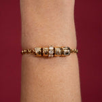 Gold bracelet with diamond accents on a wrist against a red background