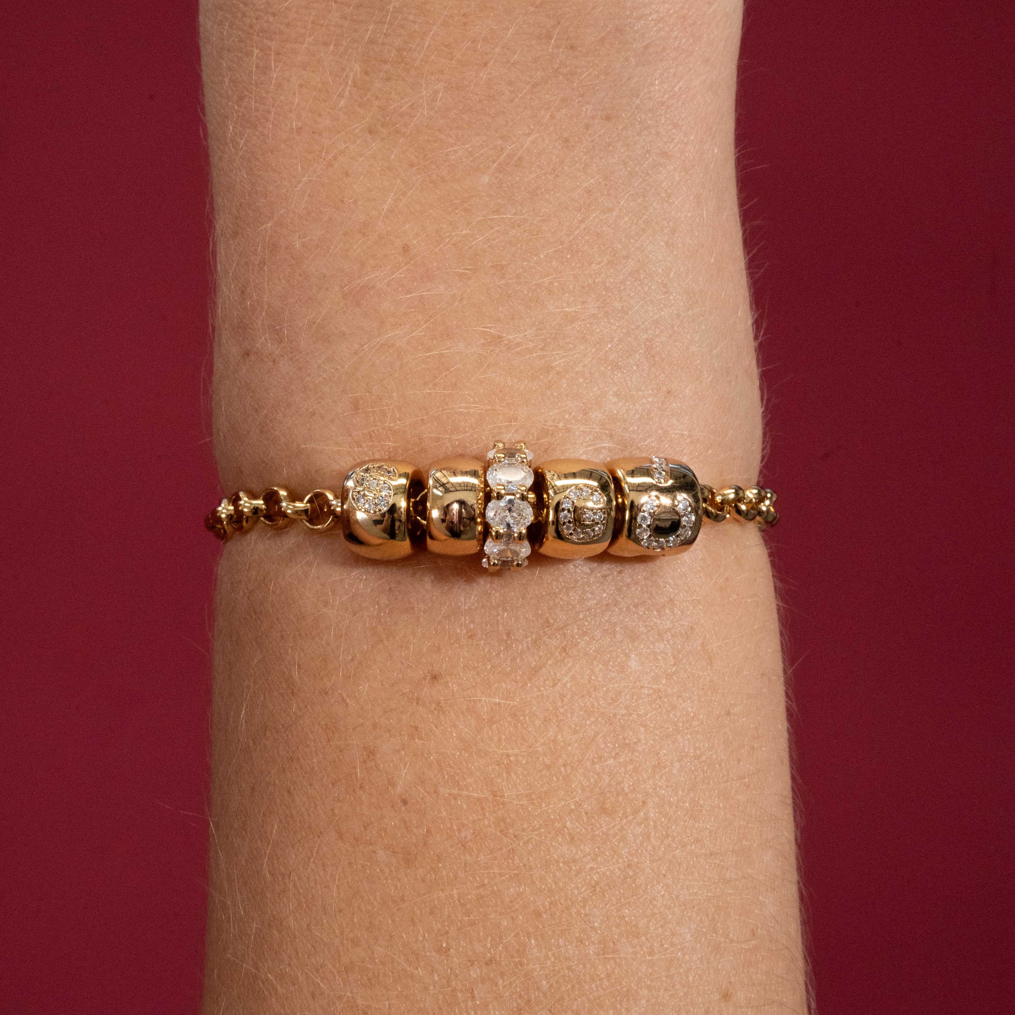 Gold bracelet with diamond accents on a wrist against a red background