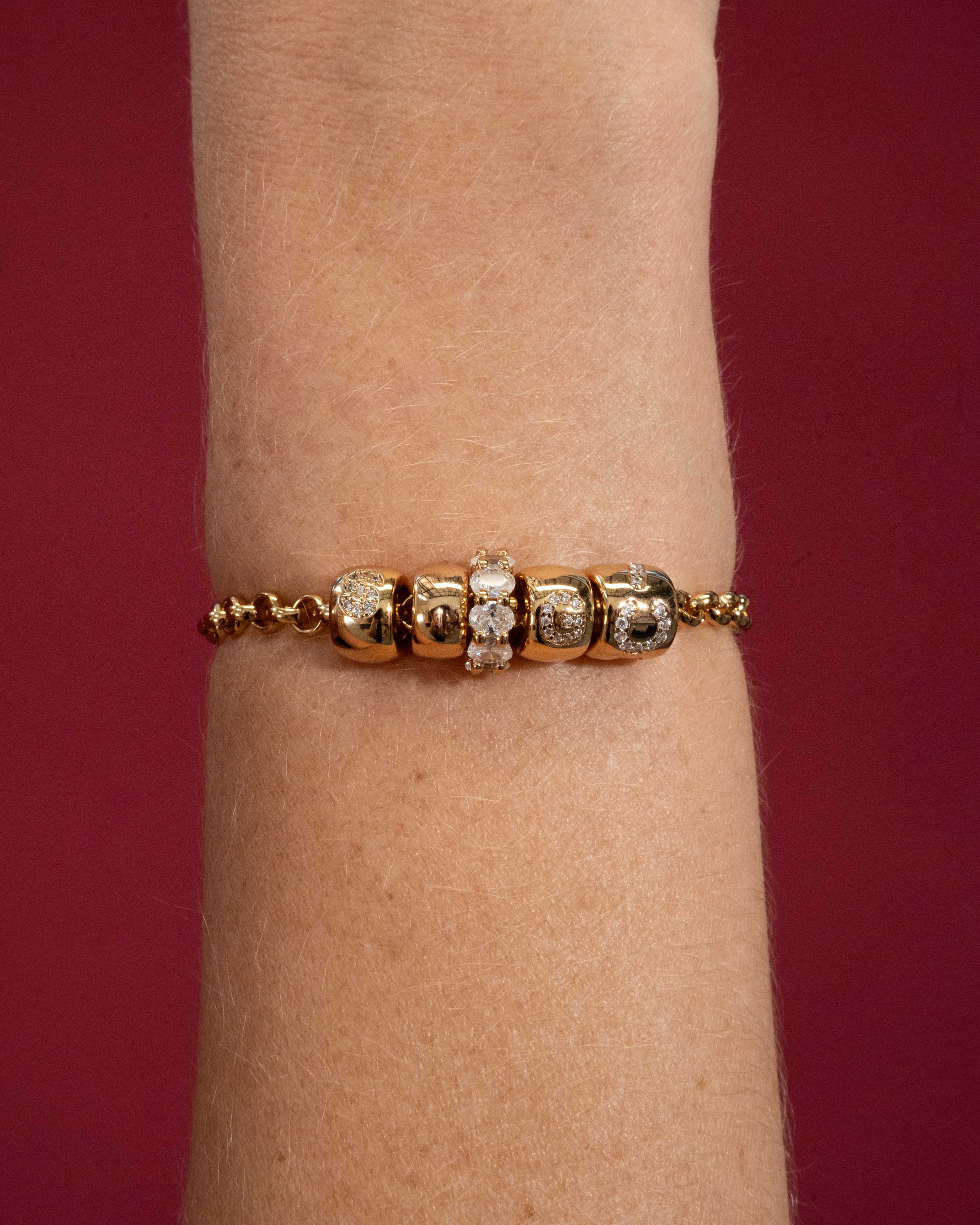 Gold bracelet with diamond accents on a wrist against a red background