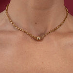 Gold belcher chain necklace on a person's neck with a red background