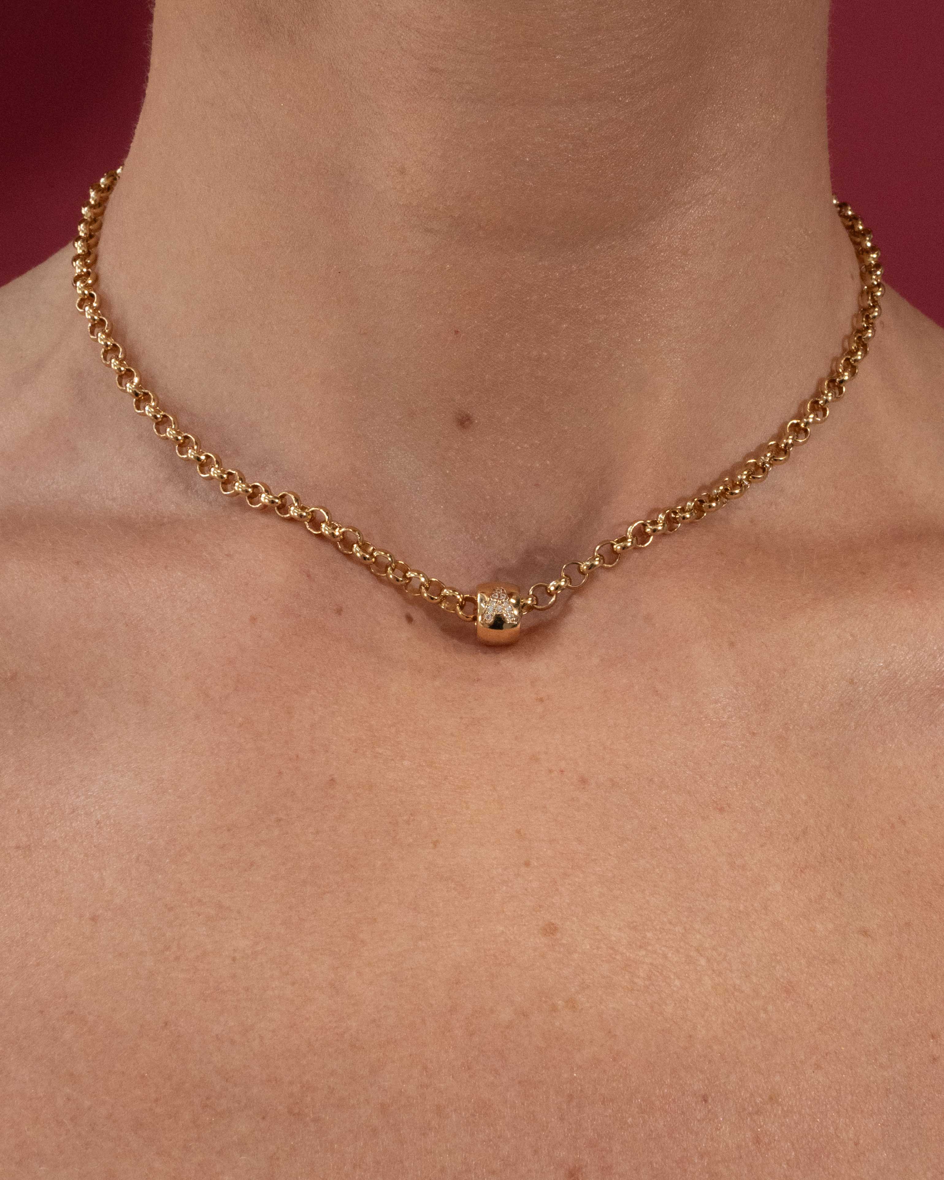 Gold belcher chain necklace on a person's neck with a red background