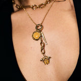 Close-up of a person wearing a gold necklace with charms on a dark background