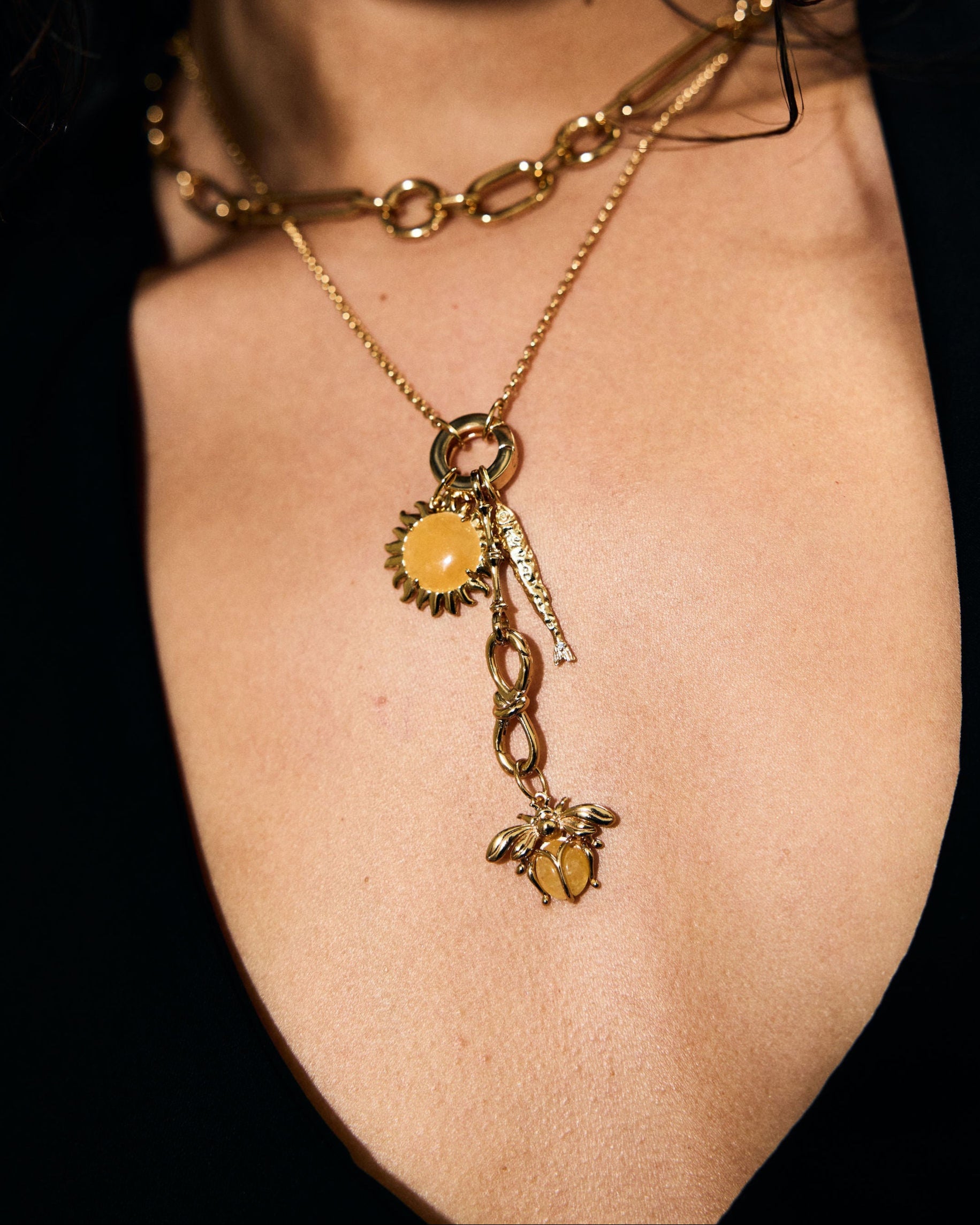 Close-up of a person wearing a gold necklace with charms on a dark background