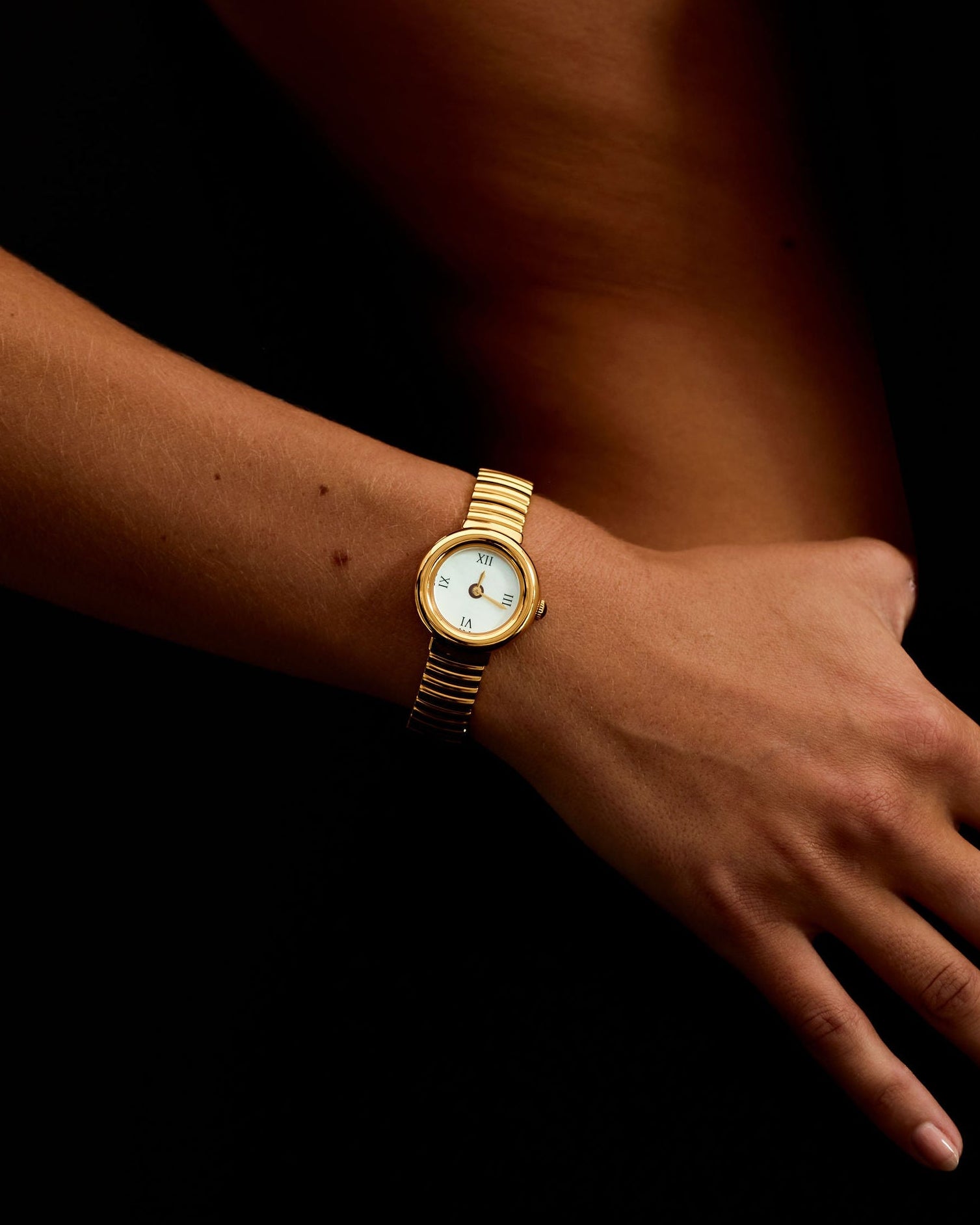 Gold wristwatch on a wrist with a dark background