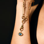 Gold chain necklace with an eye-shaped pendant on a person's arm against a black background
