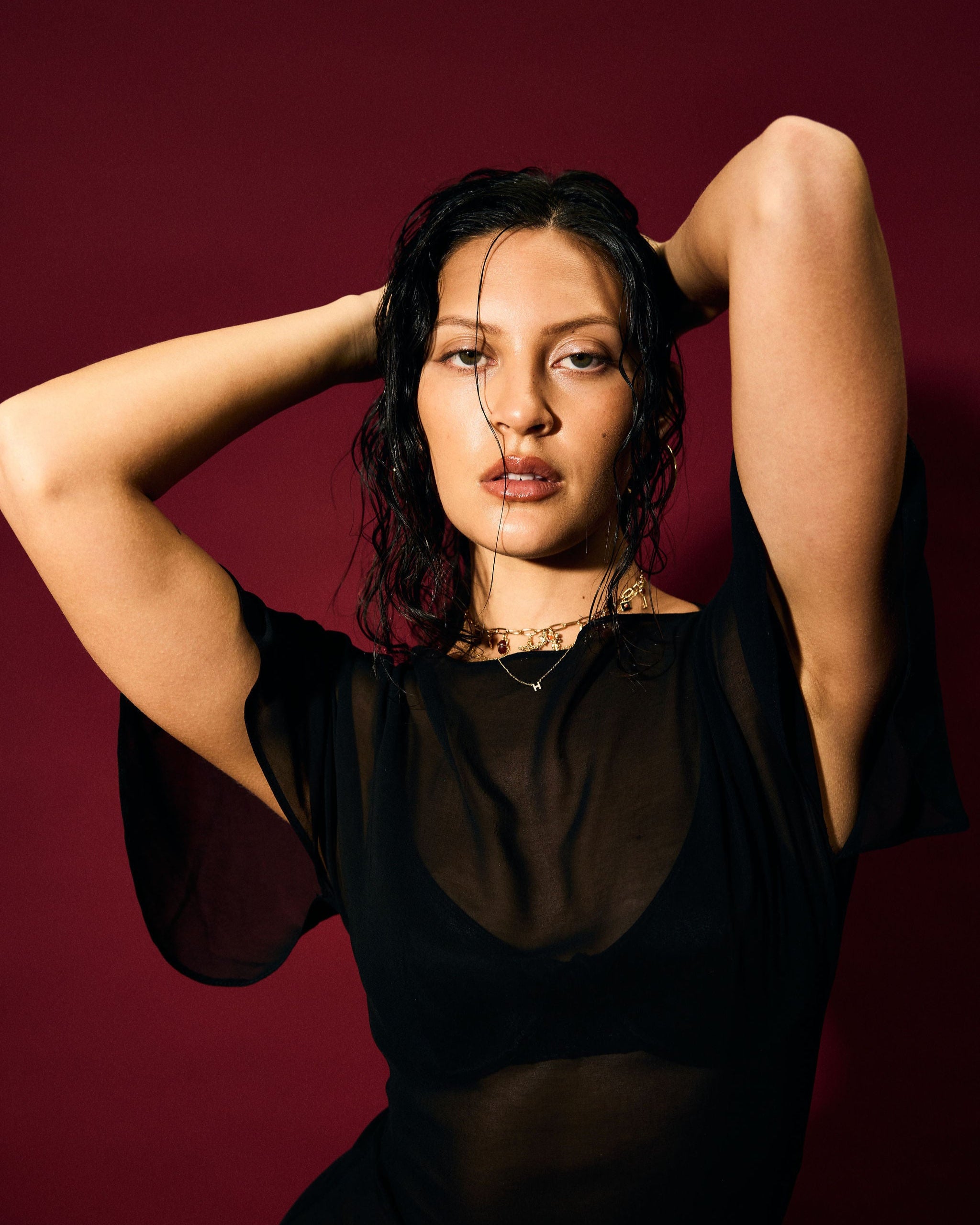 Woman posing with hands behind head against a dark red background