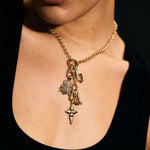 Close-up of a person wearing a gold necklace with charms against a black background