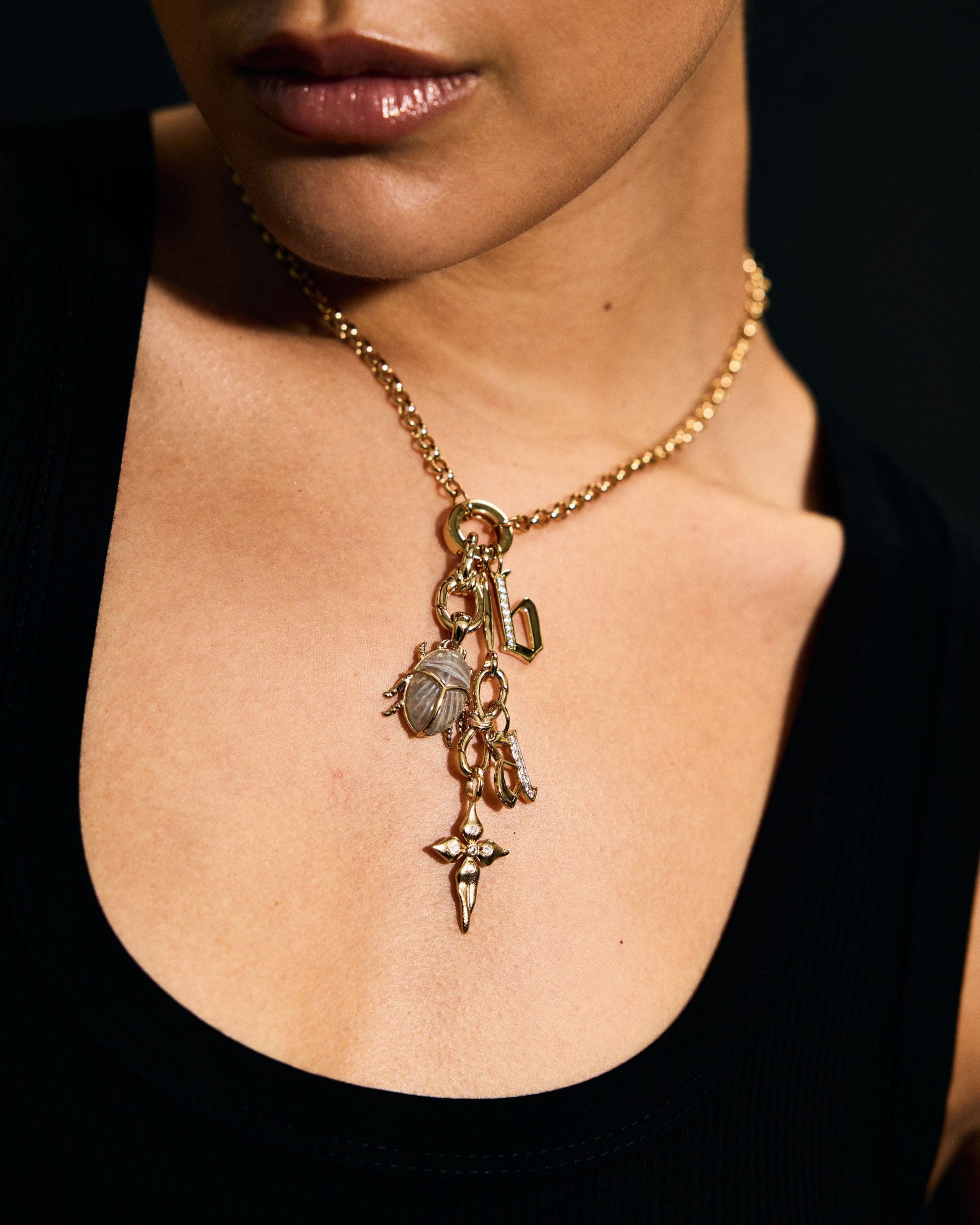 Close-up of a person wearing a gold necklace with charms against a black background