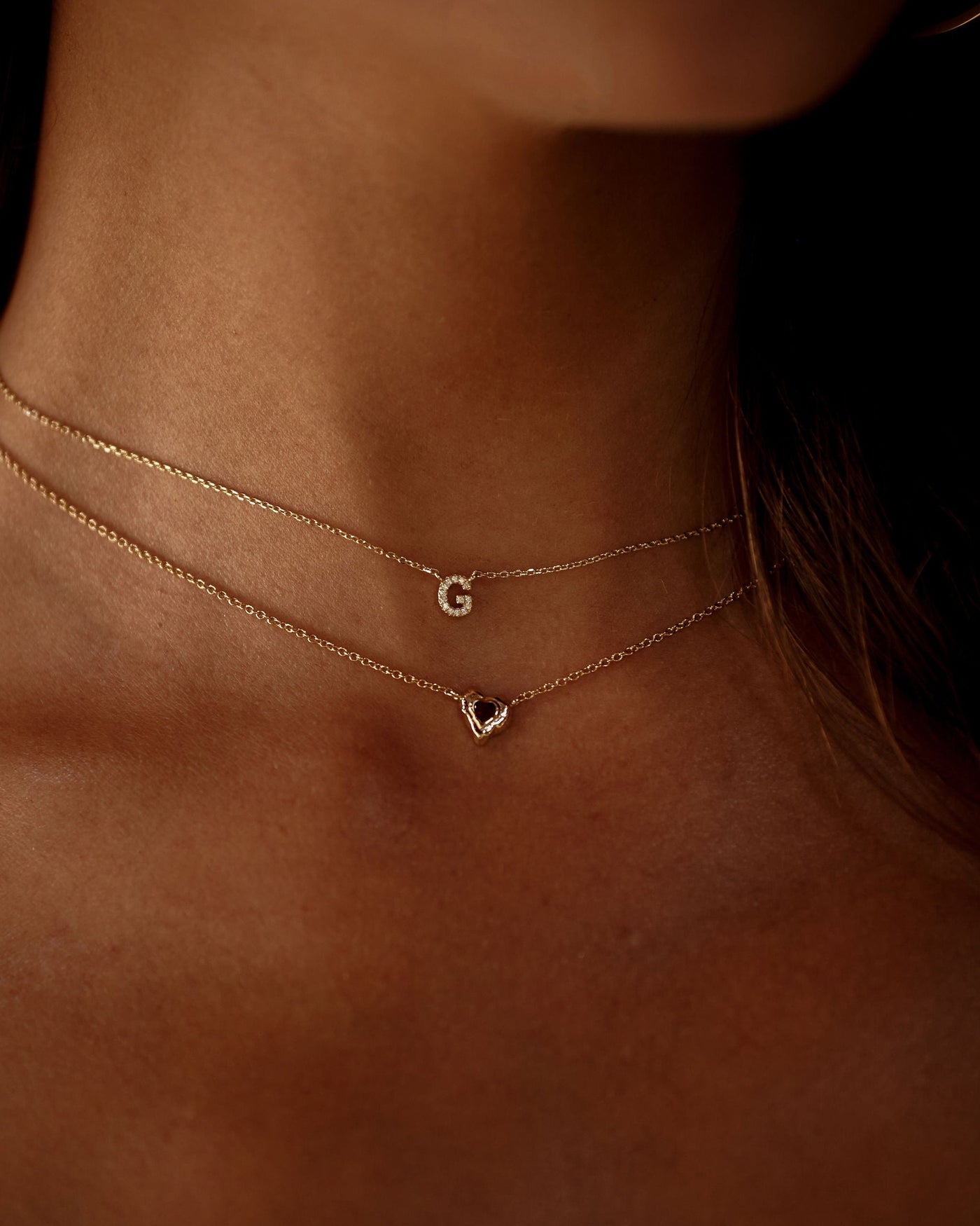 Close-up of a person wearing two delicate necklaces with small pendants on a dark background