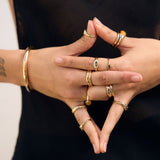 Close-up of hands with multiple gold rings and bracelets on a black background