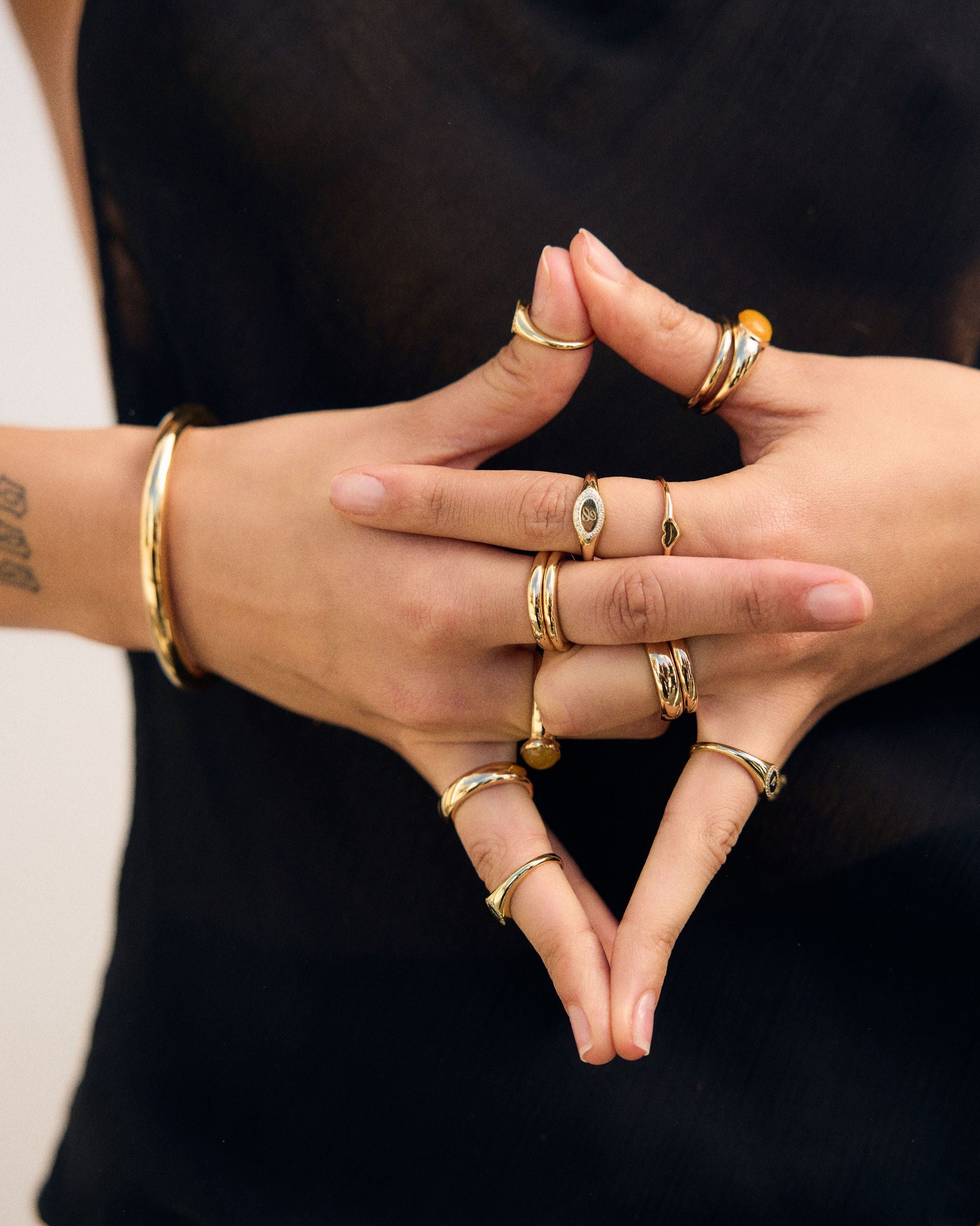 Close-up of hands with multiple gold rings and bracelets on a black background