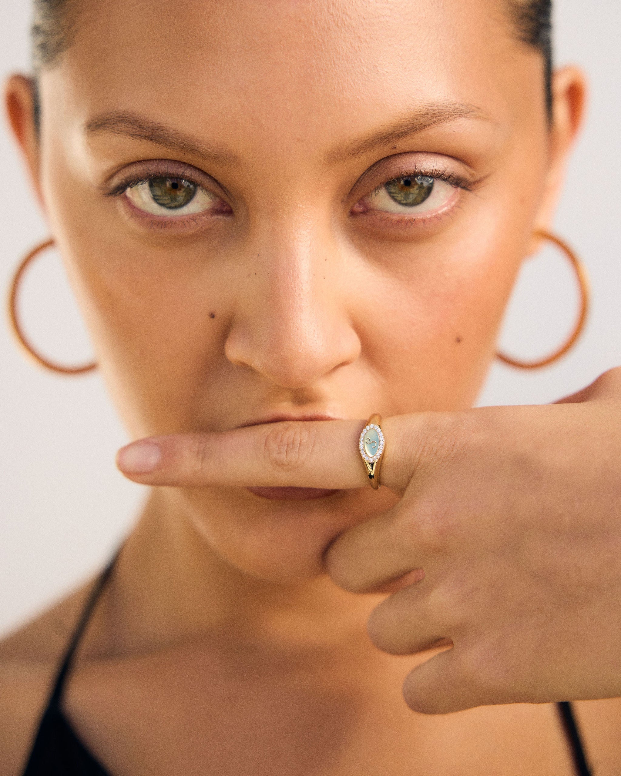 Close-up of a woman with hoop earrings and a ring, with a hand covering her mouth.