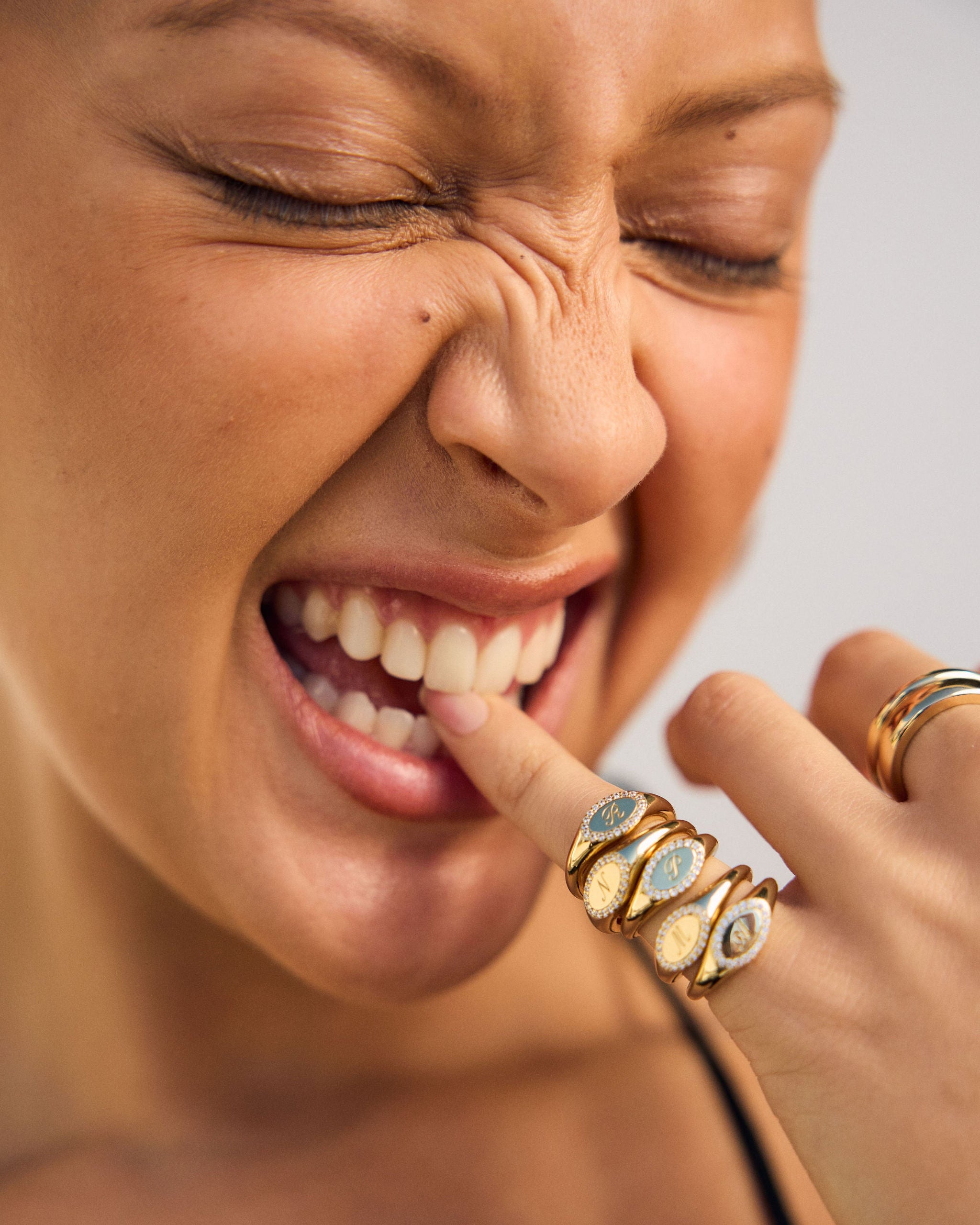 Close-up of a woman with gold rings on her fingers, pointing to her teeth.