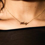 Gold necklace with 'Lucky' pendant on a person wearing a black top.