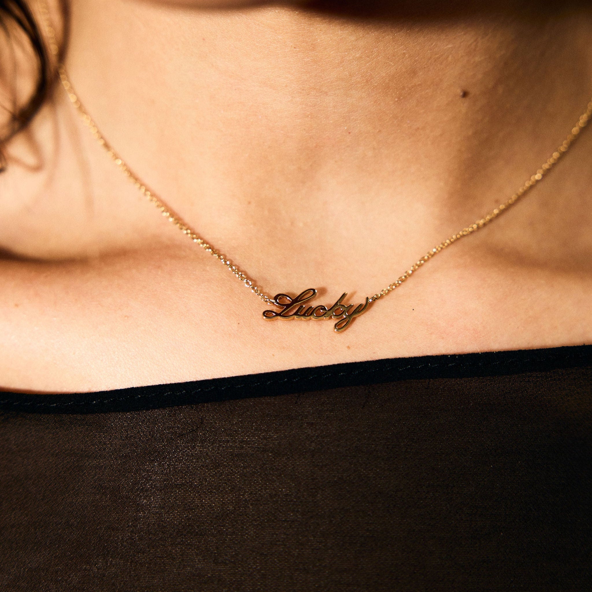 Gold necklace with 'Lucky' pendant on a person wearing a black top.