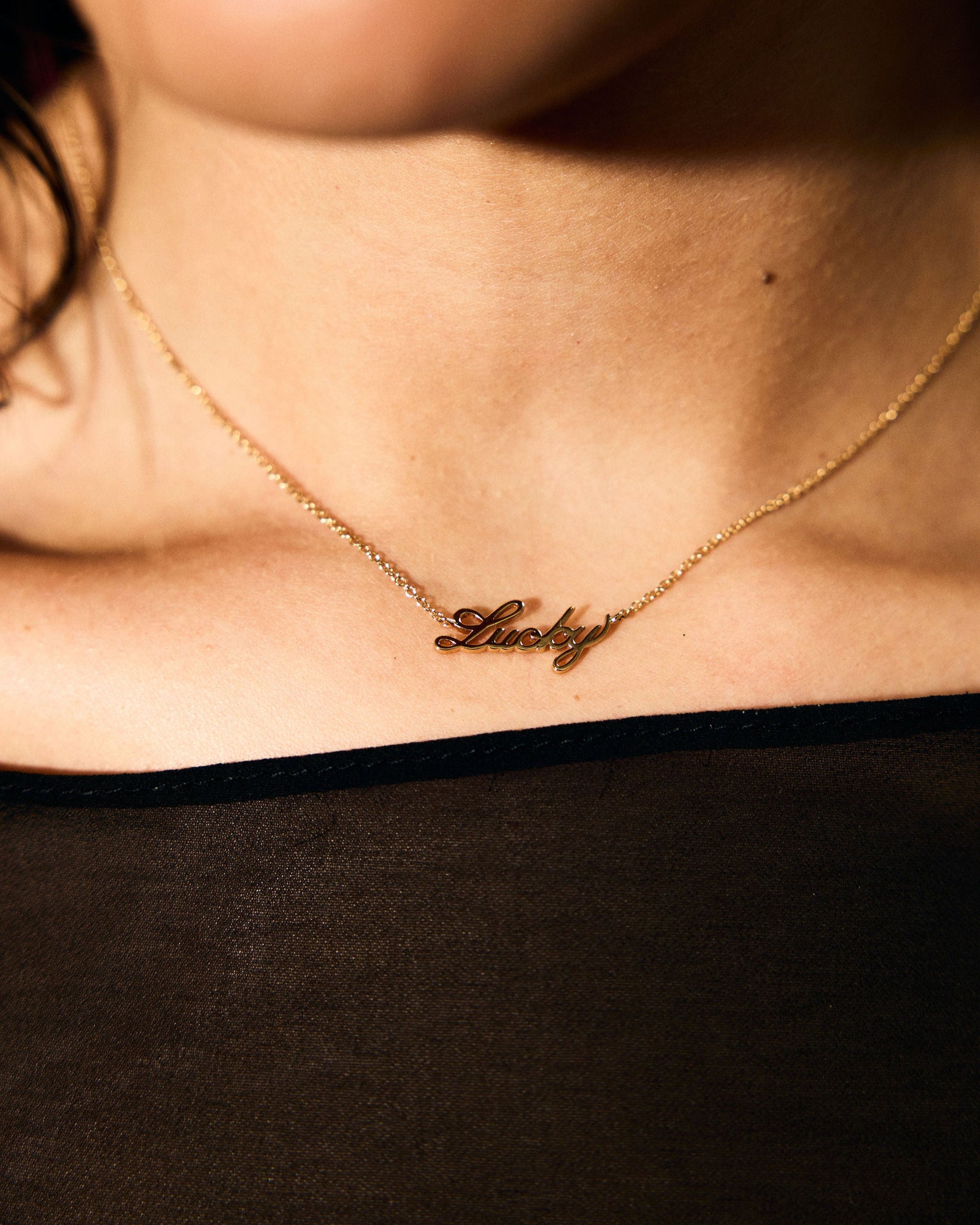 Gold necklace with 'Lucky' pendant on a person wearing a black top.