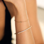 Close-up of a person's arm wearing gold a fine letter and tennis bracelet