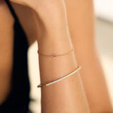 Close-up of a person's arm wearing gold a fine letter and tennis bracelet