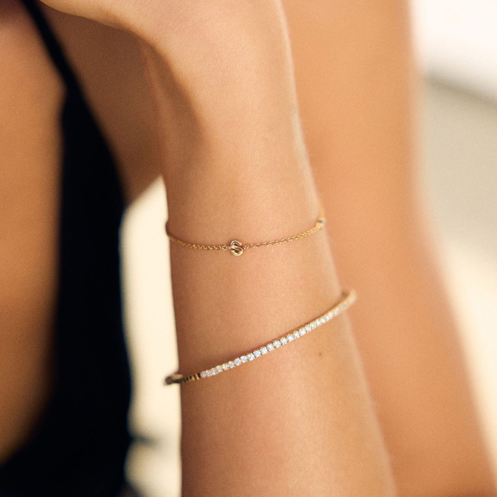 Close-up of a person's arm wearing gold a fine letter and tennis bracelet