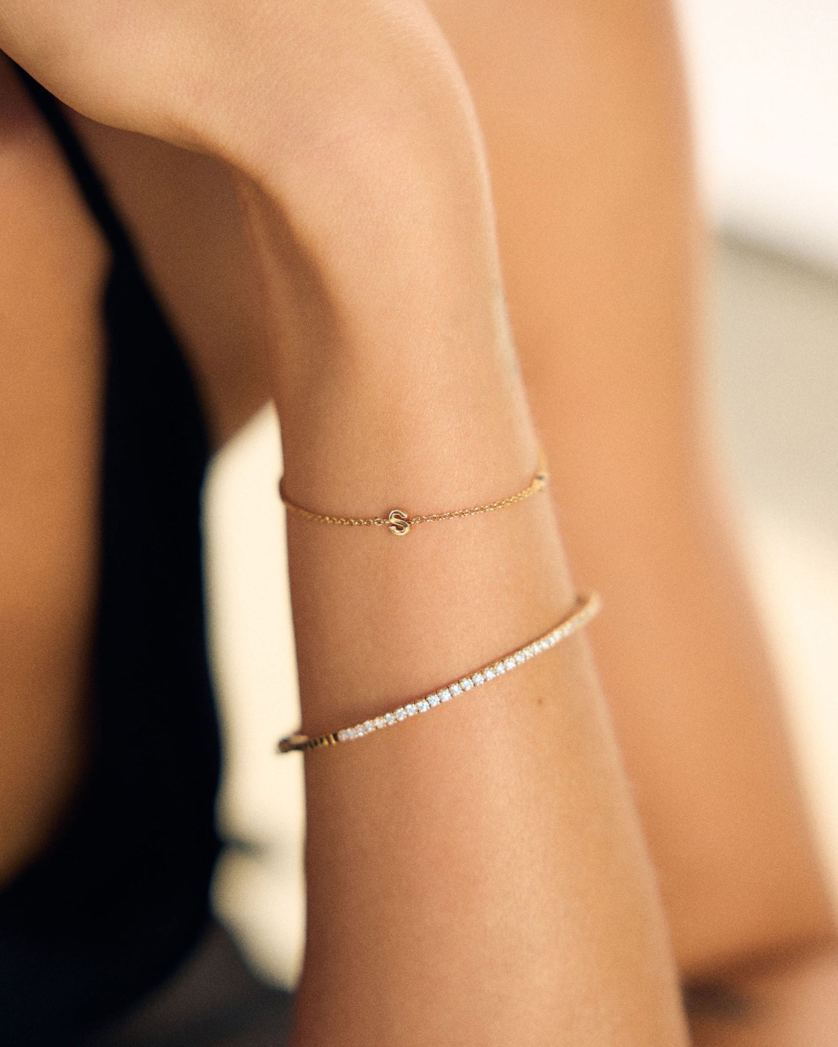 Close-up of a person's arm wearing gold a fine letter and tennis bracelet