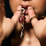 Close-up of a person holding a gold necklace with a red gemstone pendant.
