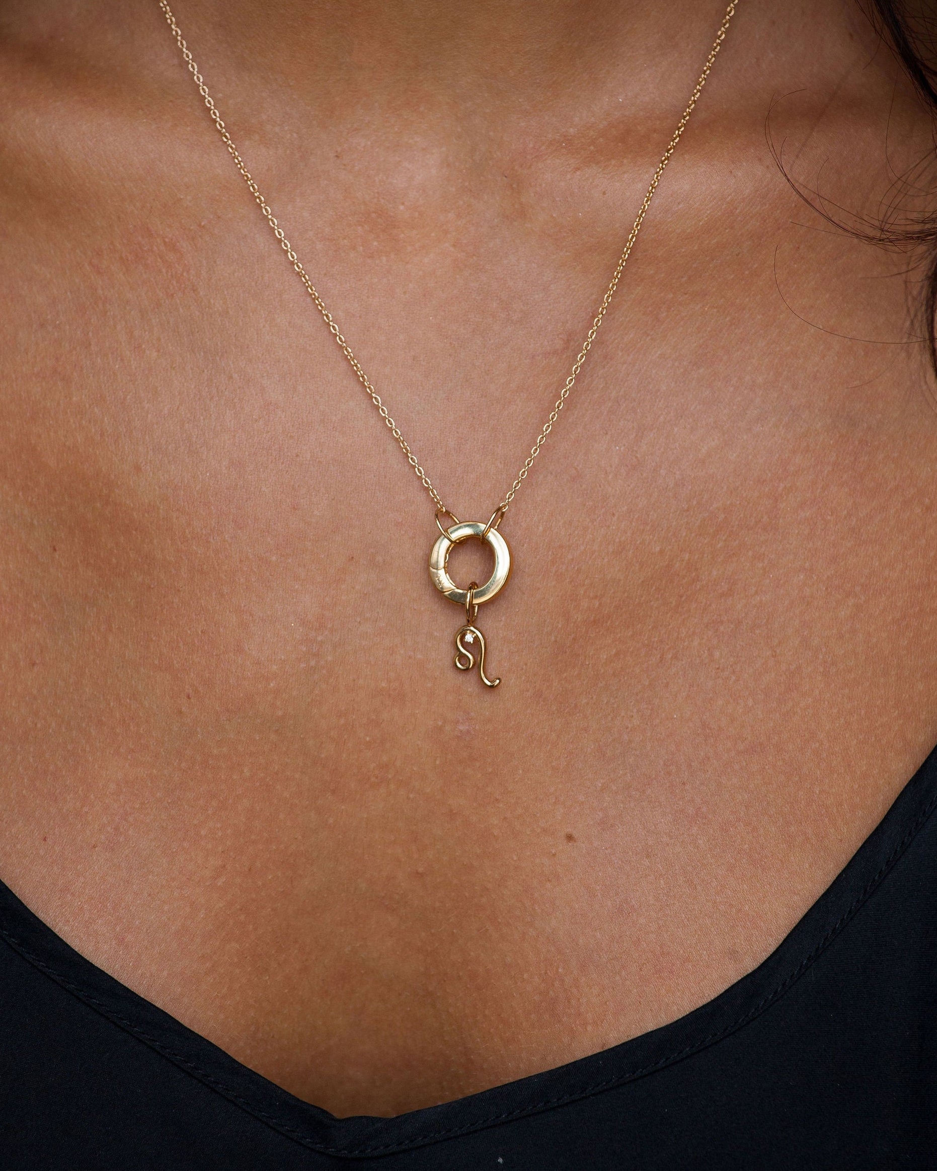 Gold necklace with a Leo pendant on a person wearing a black top.