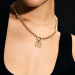 Close-up of a person wearing a gold necklace with a 'M' pendant against a dark background