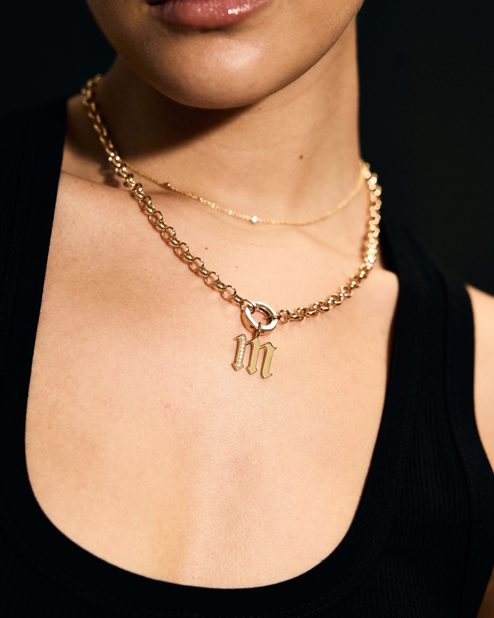 Close-up of a person wearing a gold necklace with a 'M' pendant against a dark background