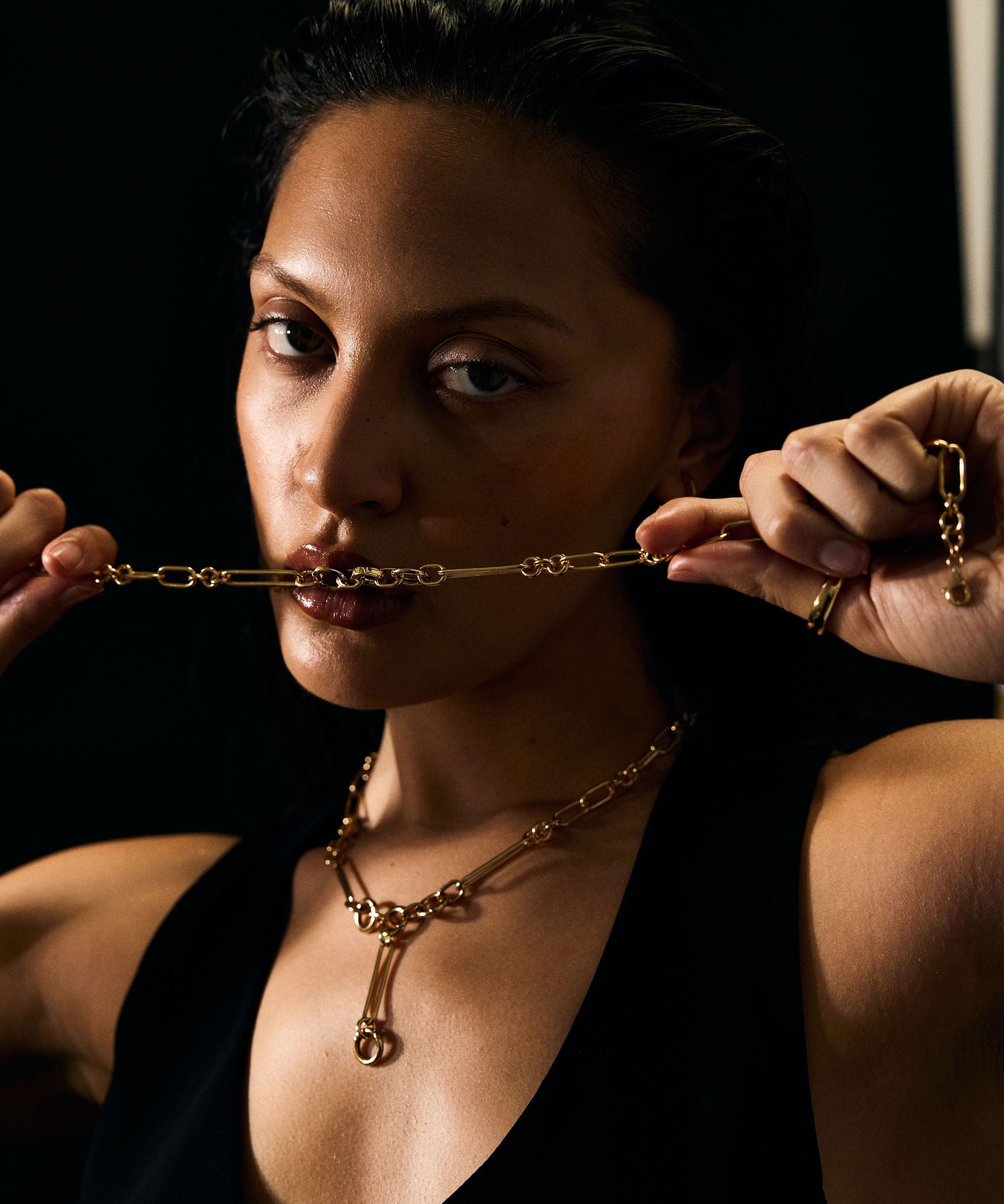 Woman wearing a gold necklace against a dark background