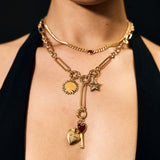 Close-up of a person wearing a gold necklace with various charms against a black background