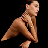 Woman wearing a gold watch and earrings against a black background
