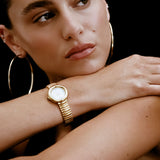 Woman wearing a gold watch and hoop earrings against a black background