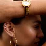 Close-up of a person wearing a gold watch and hoop earrings with a dark background