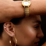 Close-up of a person wearing a gold watch and hoop earrings with a dark background