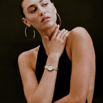 Woman wearing gold hoop earrings and a watch on a dark background
