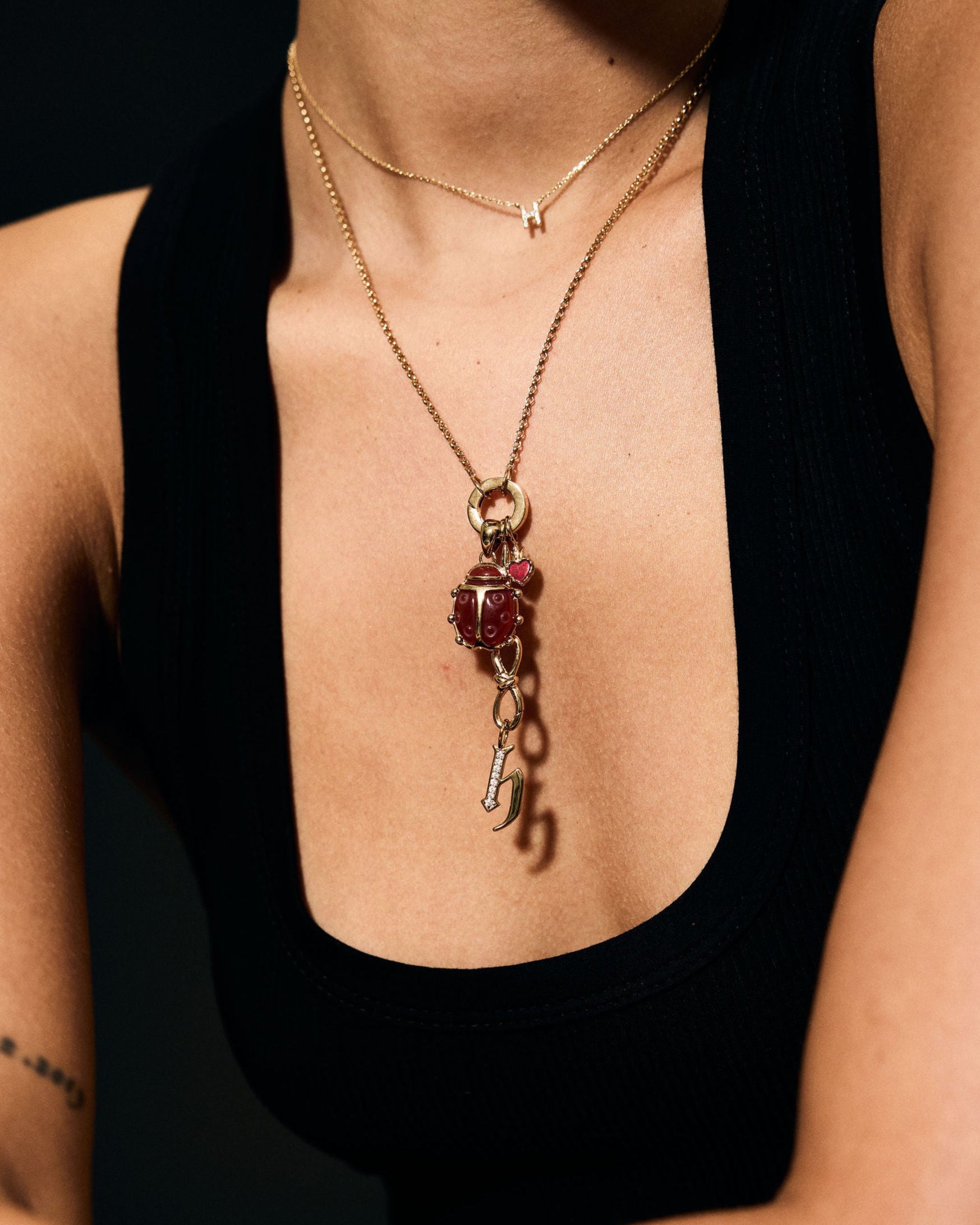 Person wearing a gold necklace with a pendant on a black background