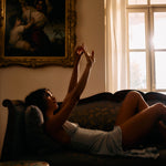 Woman lying on a couch with a painting and window in the background