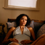 Woman sitting on a couch in a dimly lit room with a window in the background