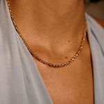 Gold chain necklace on a person wearing a light gray top.