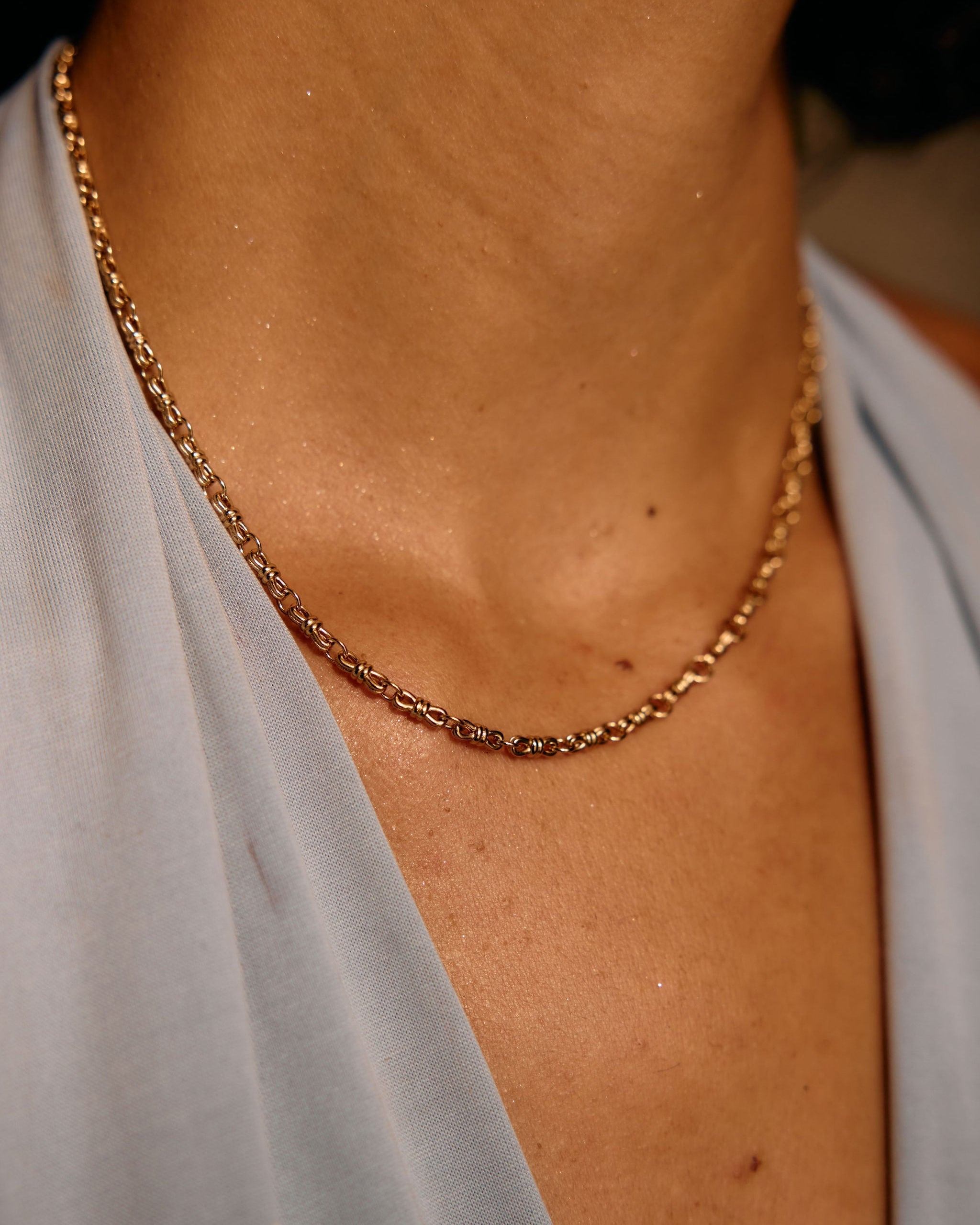 Gold chain necklace on a person wearing a light gray top.