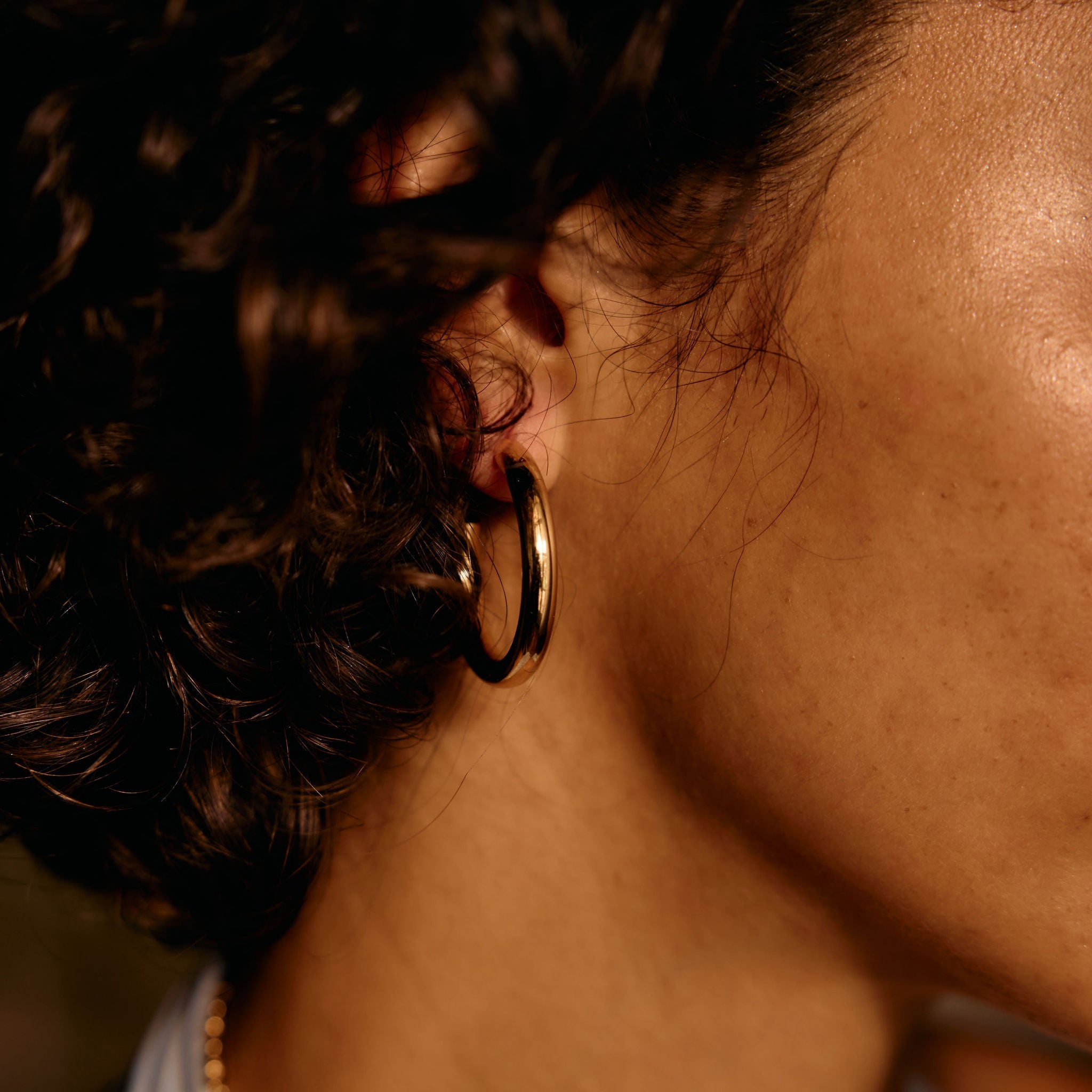 Close-up of an ear with gold hoop earrings and a blurred background