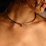 Close-up of a person wearing a gold necklace with a clear gemstone.