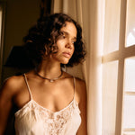Woman wearing a lace-trimmed nightgown by a window with soft lighting