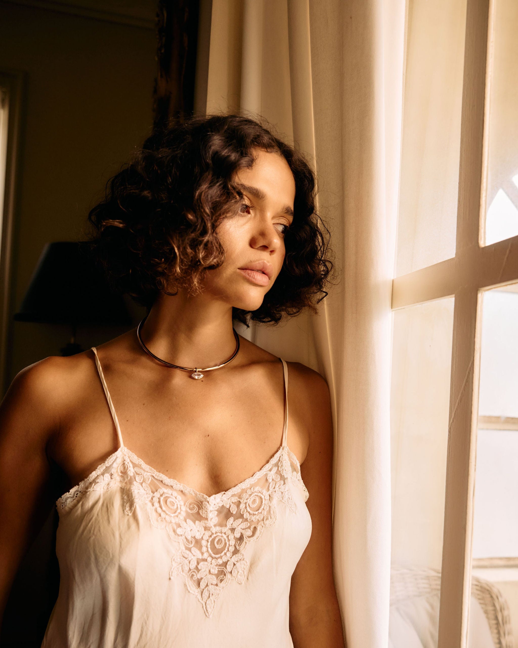 Woman wearing a lace-trimmed nightgown by a window with soft lighting