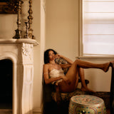 Woman sitting by a fireplace in a warm, sunlit room.