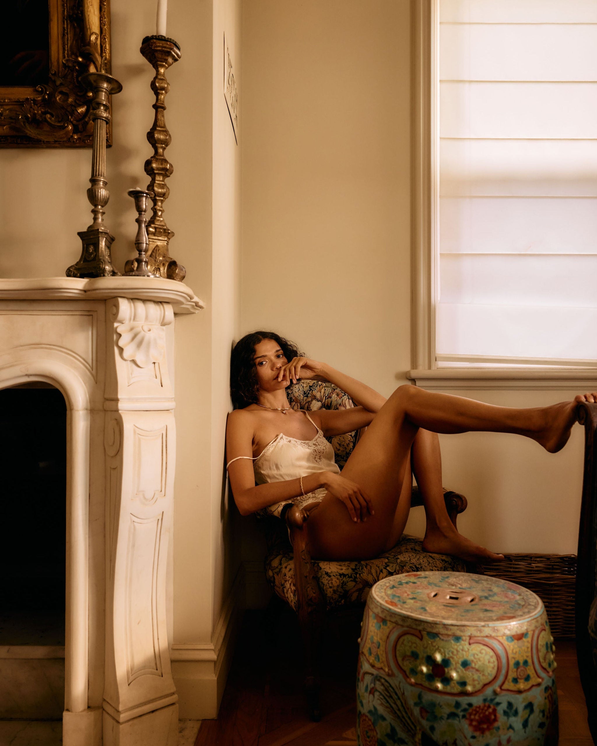 Woman sitting by a fireplace in a warm, sunlit room.