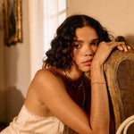 Woman in a white lace nightgown sitting on a chair in a warmly lit room.