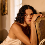 Woman in a white lace nightgown sitting on a chair in a warmly lit room.