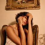 Woman sitting on a chair with a painting of flowers on the wall behind her